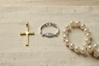 Bijoux chrétiens haut de gamme disposés sur lin crème : croix en or, bracelet ichthus en argent et chapelet en perles, détails de finition visibles